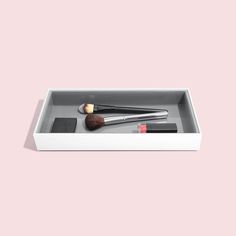 an empty white box with two brushes in it on a pink background that is also used as a makeup brush holder