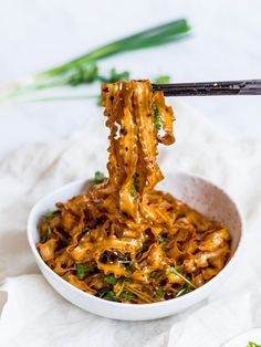 noodles being lifted from a bowl with chopsticks over it and another dish in the background