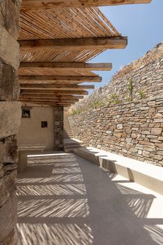 an outdoor area with stone walls, benches and pergolated roofing on the side