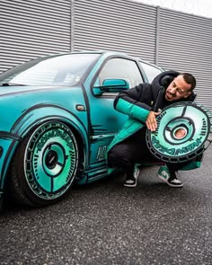 a man sitting on the hood of a car holding a skateboard in front of his face