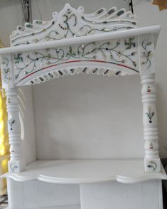 a white shelf with an ornate design on it's sides and shelves below the shelf