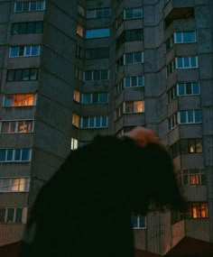 a person standing in front of a tall building at night with windows lit up behind them