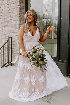 a woman in a white dress holding a bouquet and posing for the camera with her hand out