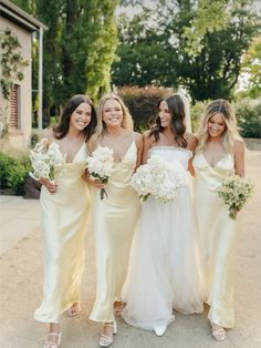 four bridesmaids in yellow dresses posing for the camera with their bouquets on