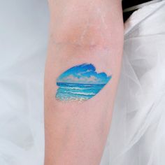 a woman's arm with a watercolor painting on it that has a wave coming in