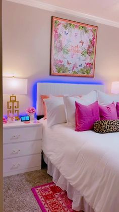 a white bed topped with lots of pillows next to a wall mounted art above it