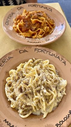 two plates with different types of pasta on them sitting on a table next to each other