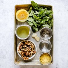 ingredients for a healthy salad laid out on a baking sheet, including spinach leaves and lemon wedges