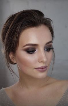 a woman with dark makeup looks down at the camera while wearing a gray top and silver eyeliners