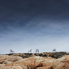 three chairs sitting on top of rocks under a blue sky