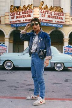 a man standing in front of a movie theater next to a blue car and holding a camera