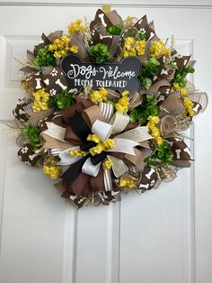 a welcome wreath with yellow flowers and brown ribbon hanging on a white front door that says dog welcome