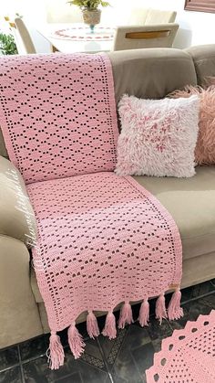 a pink crocheted afghan sitting on top of a couch next to two pillows