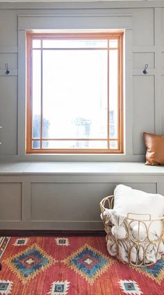 a room with a bench, window and rug on the floor