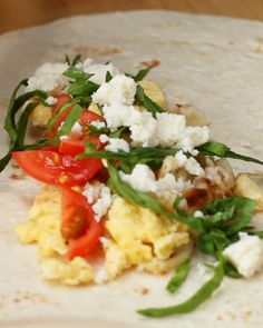 an uncooked tortilla with tomatoes, cheese and spinach on it