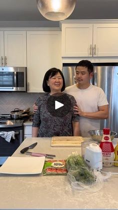 a man and woman standing in a kitchen next to an island with food on it