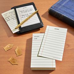 three notebooks and two pieces of paper on a table next to an open book