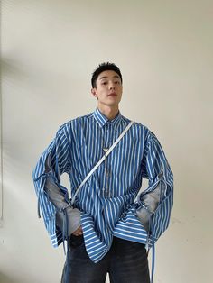 This shirt features a striped fabric with exceptional texture and color. The sleeves have a unique design with gray T-shirt sleeves on the inside layer, while the outer layer has ties that can be left open or crossed and tied. The fit is loose and comfortable. Fabric composition: 100% Cotton. Model's measurements: Height 184cm, Weight 72kg, wearing size XL. Studio Weave, Long Sleeve Layer, Oversized Button Down Shirt, Loose Fit Blouse, Dapper Dan, Loose Fit Shirts, Studio Blue, Striped Fabric, Streetwear Men Outfits