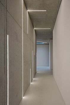 an empty hallway with white walls and light coming from the ceiling, leading to another room