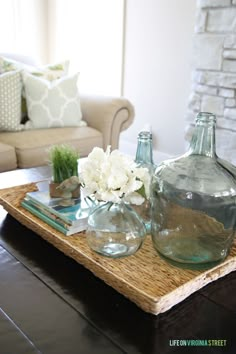 three glass vases on a coffee table with white flowers in them and some books