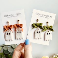 two handmade ghost earrings with bows on them, one being held up to the camera