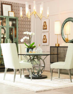 a dining room table with white chairs and a round mirror on the wall above it