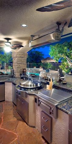 an outdoor kitchen with stainless steel appliances and granite counter tops at night, overlooking the pool