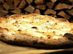 a pizza sitting on top of a wooden table next to stacks of firewood in the background