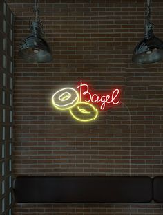 a neon sign that says bagel on the side of a brick wall next to two lamps