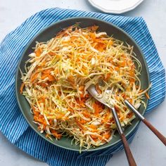 shredded carrots and cabbage in a bowl on a blue towel with two spoons