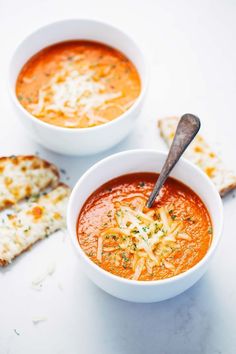 two bowls of tomato soup with crackers on the side