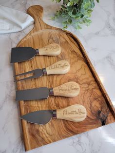 four knives are sitting on a wooden cutting board with engraved names and numbers, along with a plant