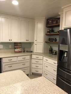 a black refrigerator freezer sitting inside of a kitchen next to white cabinets and counter tops