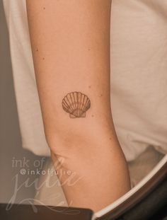 a woman's arm with a small tattoo of a shell on her left side