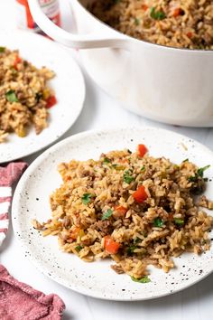 two plates filled with rice and vegetables on top of a white table next to a red striped napkin