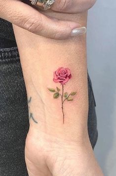 a woman's wrist with a small pink rose tattoo on the left side of her arm