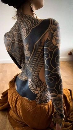 a woman with tattoos on her back sitting on the floor