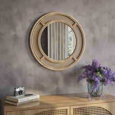 a vase with purple flowers sitting on top of a wooden table next to a mirror