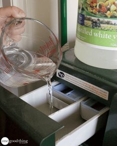 a person pouring water into a glass in front of a container on top of a counter