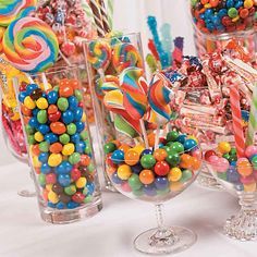 a table topped with lots of candy and lollipops in glass vases