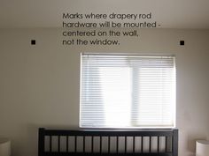 there is a bed with a black headboard and white sheets in the room that says marks where drapery rod hardware will be mounted - centered on the wall, not the window