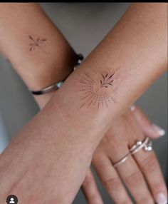 two hands holding each other with small tattoos on their arm and wrist, one has a sunburst in the middle