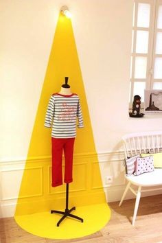 a mannequin is standing in front of a yellow triangle on a stand next to a white chair