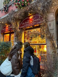 two people are standing in front of a store with christmas decorations on the windows and doors