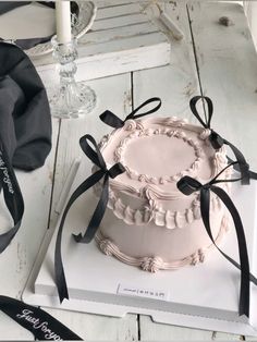 a pink cake sitting on top of a white box next to a candle and ribbon