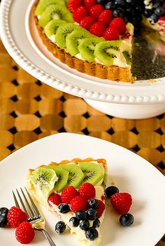 a piece of cake on a plate with berries and kiwi