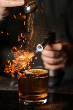 a person pouring something into a glass with a lighter in it and fire coming out of the top