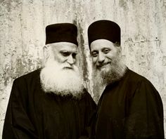 two men standing next to each other with long white beards and wearing black robes