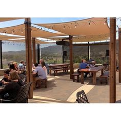 people are sitting at tables under an awning on a patio with mountains in the background