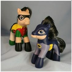 two toy figurines of batman and robin wayne on a white surface with a gray background